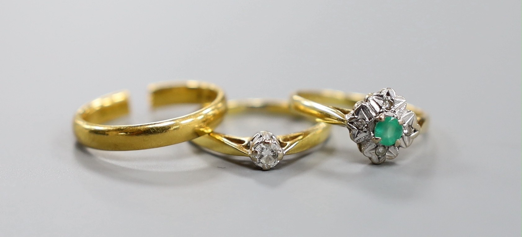 A 22ct yellow gold wedding band (cut), 3.5 grams together with two 18ct gold rings, emerald and illusion set diamond and diamond solitaire, gross 4.6 grams.